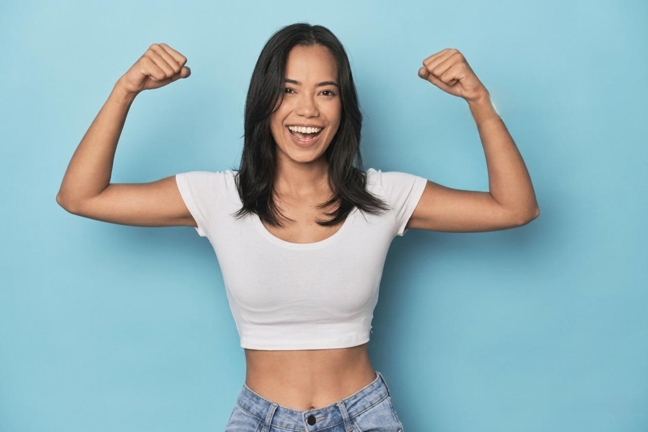 Woman flexing her arms and smiling against a light blue background.