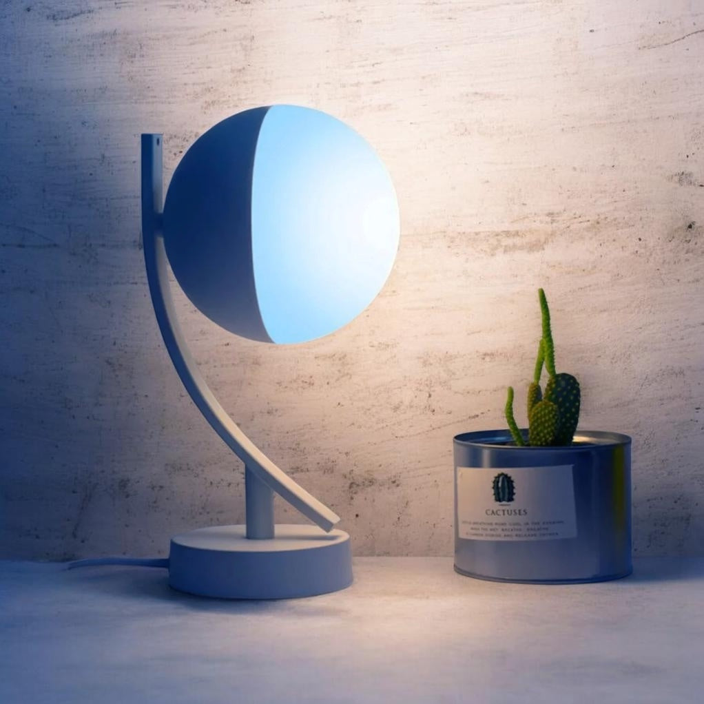 A modern lamp with a blue light next to a cactus in a canister labeled 'Cactuss'.