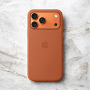 Refurbished apple device with a brown case and three rear cameras on a textured surface.